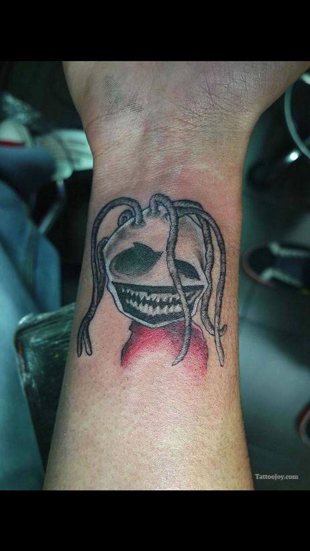 a tattoo on the wrist of a person with long hair and an alien face in it