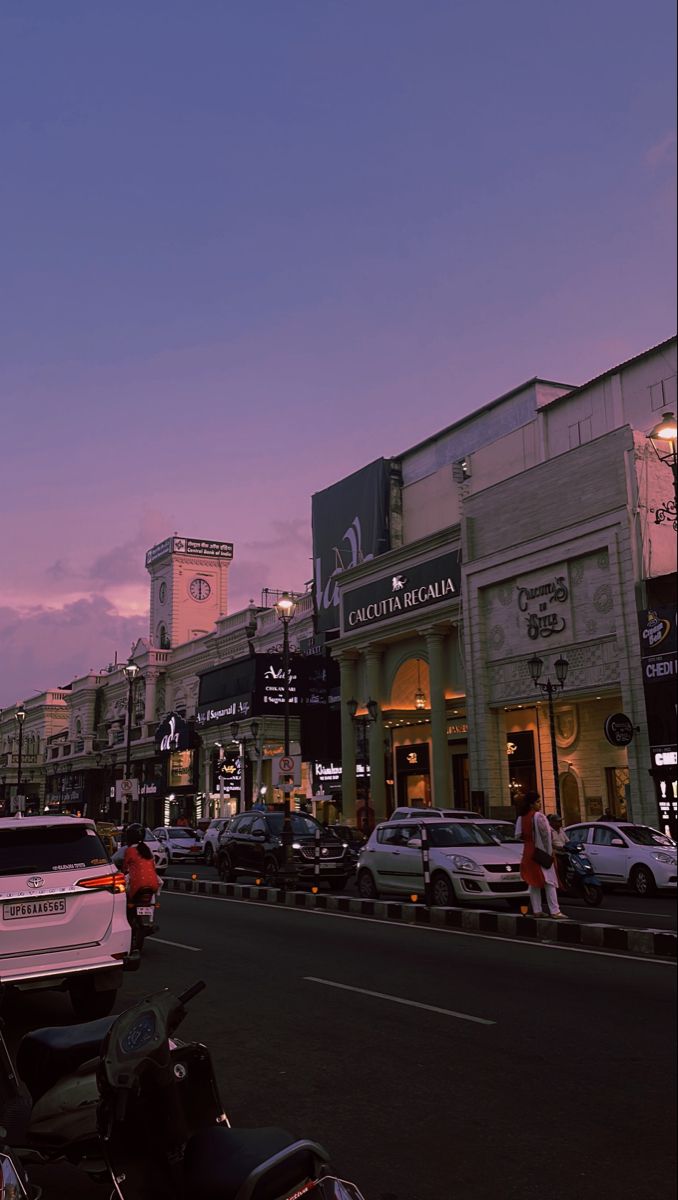 cars and motorcycles are parked on the side of the road in front of shops at dusk