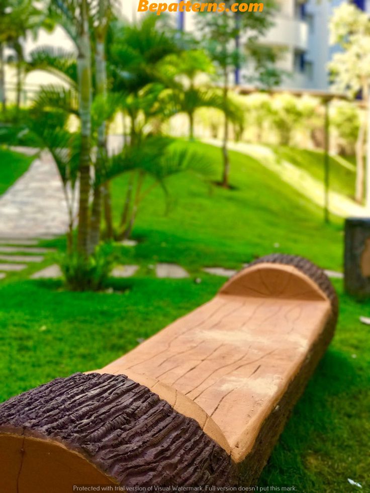 a wooden bench sitting in the middle of a lush green park with palm trees behind it