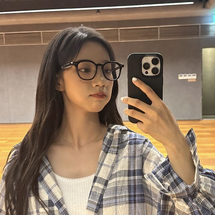 a woman wearing glasses taking a selfie with her cell phone in an empty room