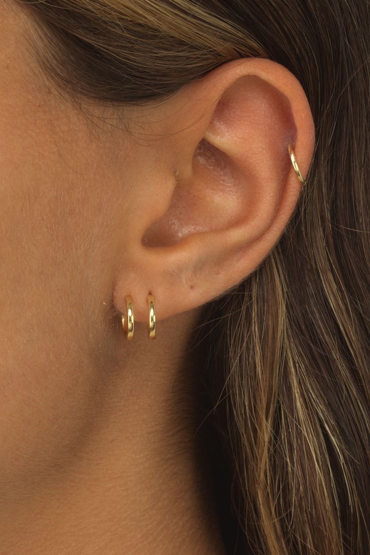 a close up of a woman's ear with two small gold earrings on it