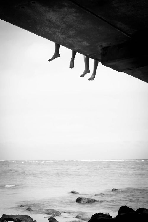 two people diving into the ocean from a pier over looking the water with their feet in the air