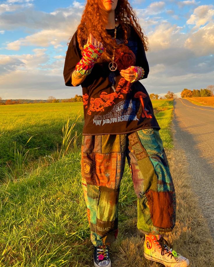 a woman standing on the side of a road with her hands in her pockets and wearing colorful pants