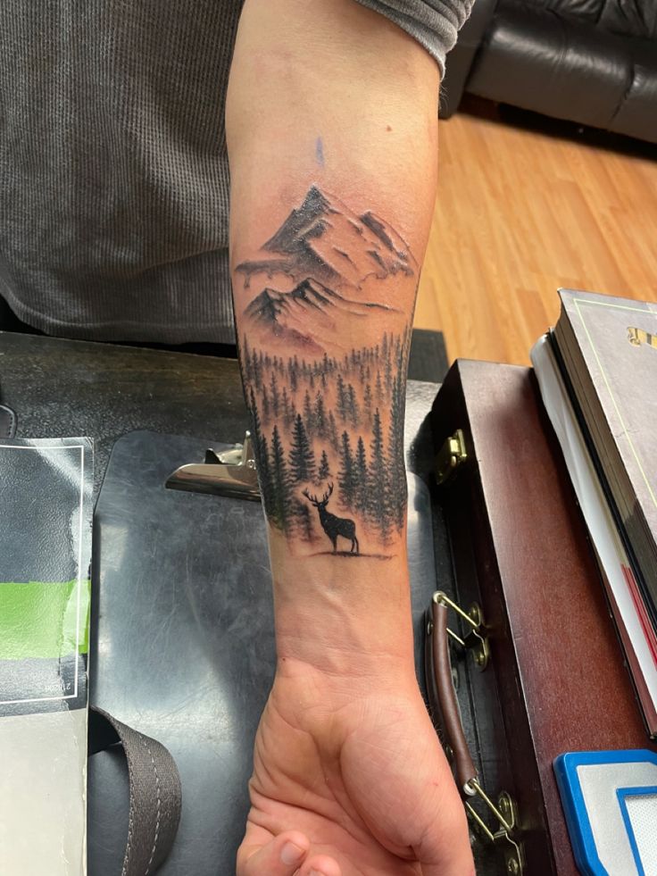 Buck silhouette standing amongst a forest with soaring mountains overlooking. Mountain Men Tattoo, Outdoors Tattoos For Guys, Moutain Tattoos Men Forearm, Elk With Mountains Tattoo, Mens Outdoors Tattoo Ideas, Men Tattoo Ideas Hunting, Outdoor Family Tattoo Ideas, Mountain And Deer Tattoo, Mountain Tatoos Men Arm