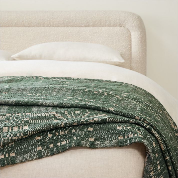 a bed with a green and white blanket on top of it next to a pillow