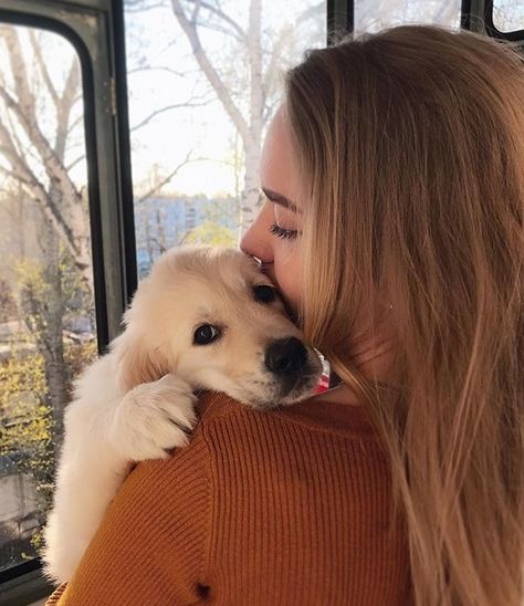 a woman holding a white dog in her arms while looking out the window at trees