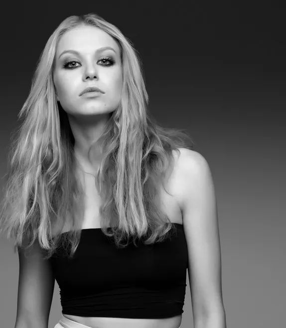 a woman with long blonde hair wearing a black top and white skirt, posing for the camera