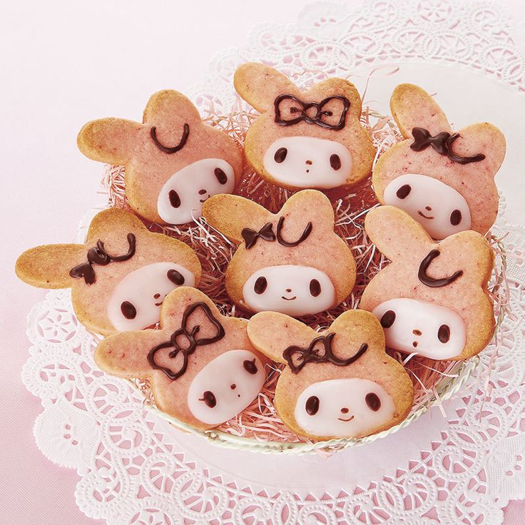 some cookies with faces on them sitting in a bowl next to lace doily and pink table cloth