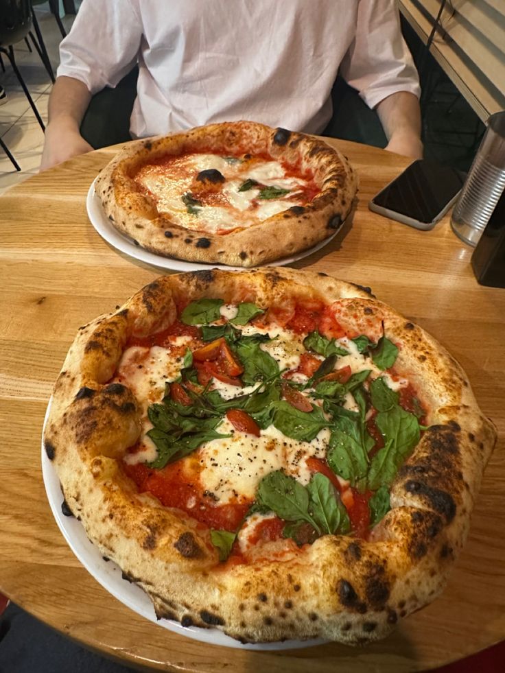 two pizzas sitting on top of white plates on a wooden table next to each other