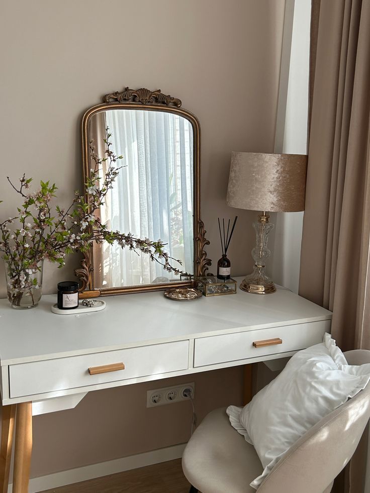 a white desk topped with a mirror next to a lamp and a vase filled with flowers