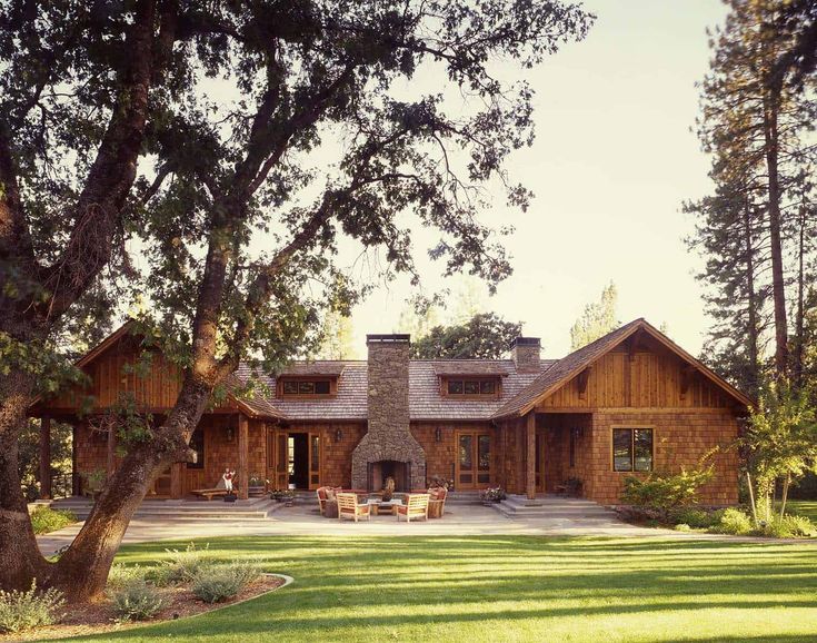 a large wooden house sitting in the middle of a lush green field next to trees