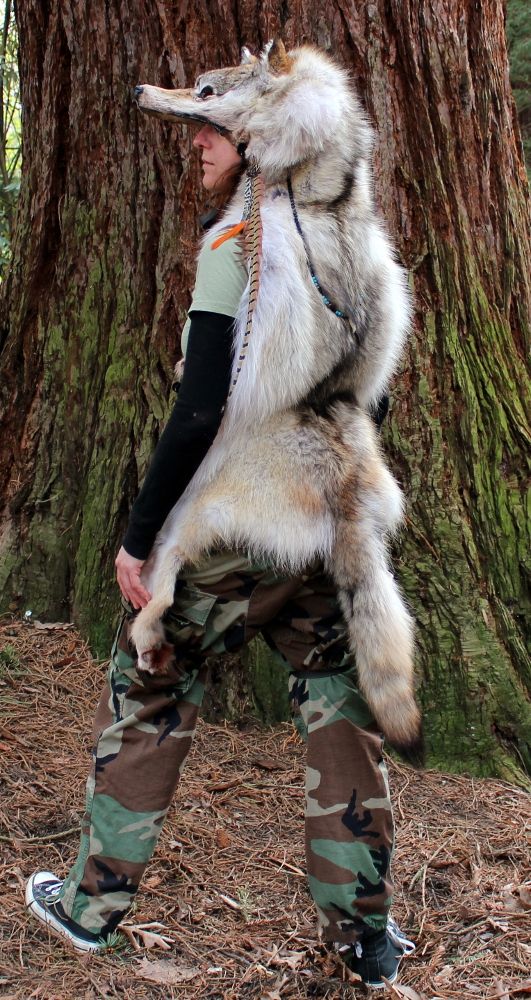 a man in camo pants holding a wolf on his back while standing next to a tree