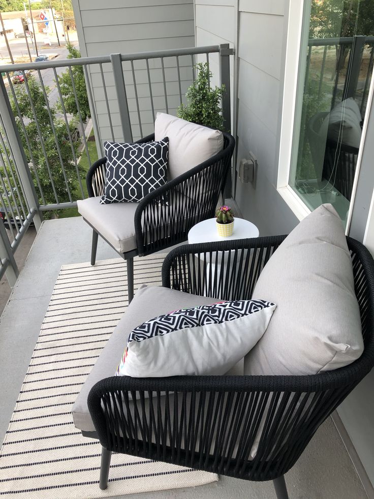 two black wicker chairs sitting on top of a porch next to a white rug