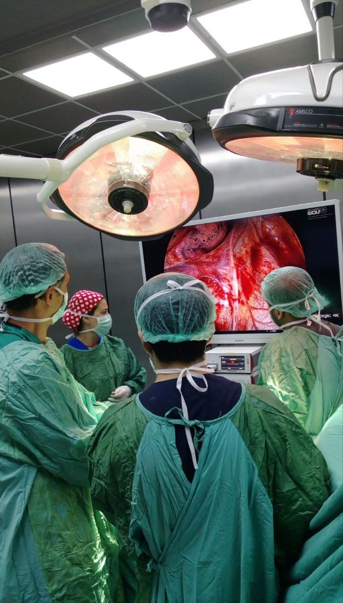 medical personnel performing surgery in an operating room with monitors on the wall and overhead lights