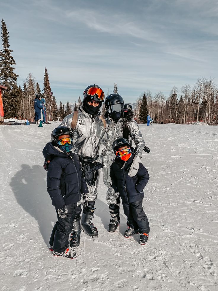 three adults and two children standing in the snow with skis on their shoulders, wearing goggles