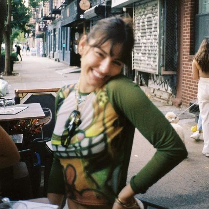 a woman standing on the sidewalk with her hands on her hips and smiling at the camera