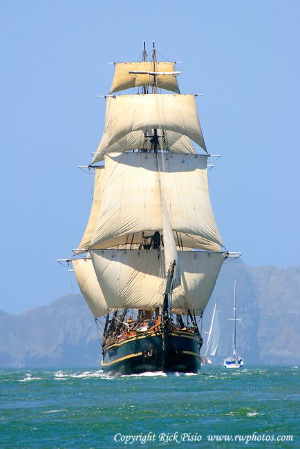 an old sailing ship in the ocean with mountains in the background