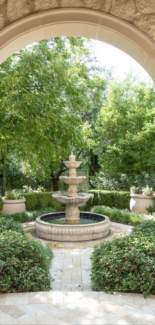 an archway leading into a garden with a fountain and potted trees in the background