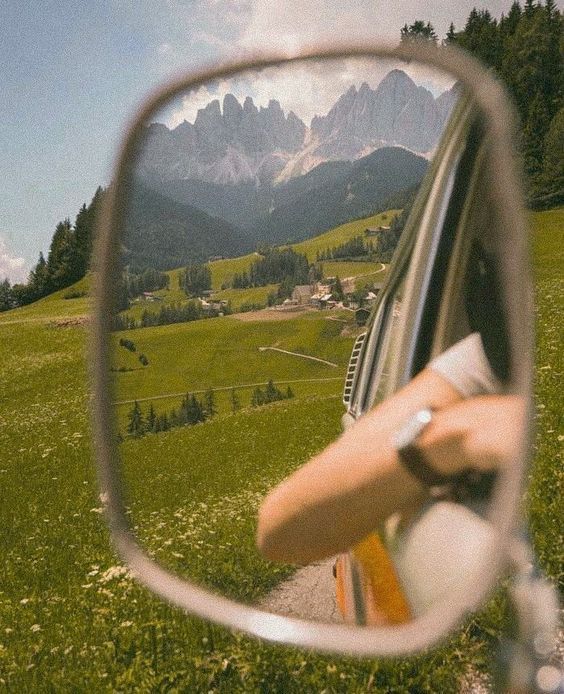 a car's side view mirror with mountains in the back ground and grass below