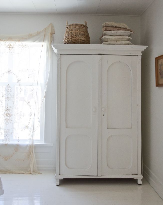 a white cabinet sitting in the corner of a room next to a window with sheer curtains