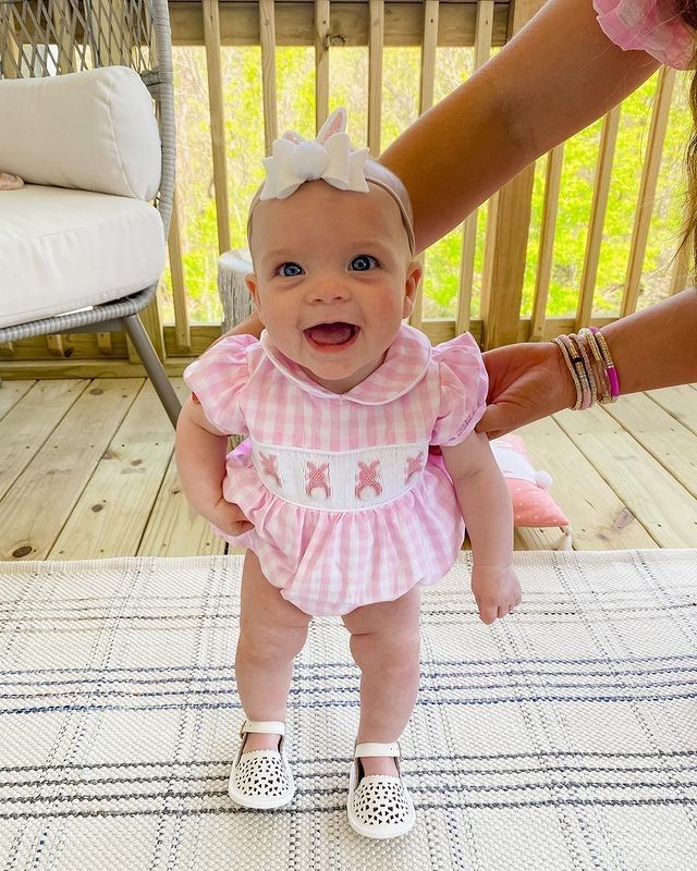 a baby girl wearing a pink dress and white shoes is being held by her mother