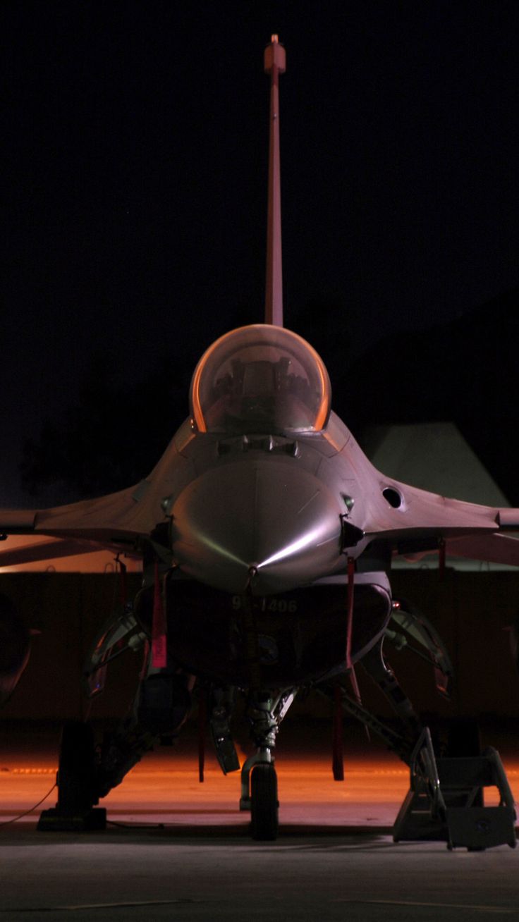 a fighter jet sitting on top of an airport tarmac at night with its lights on