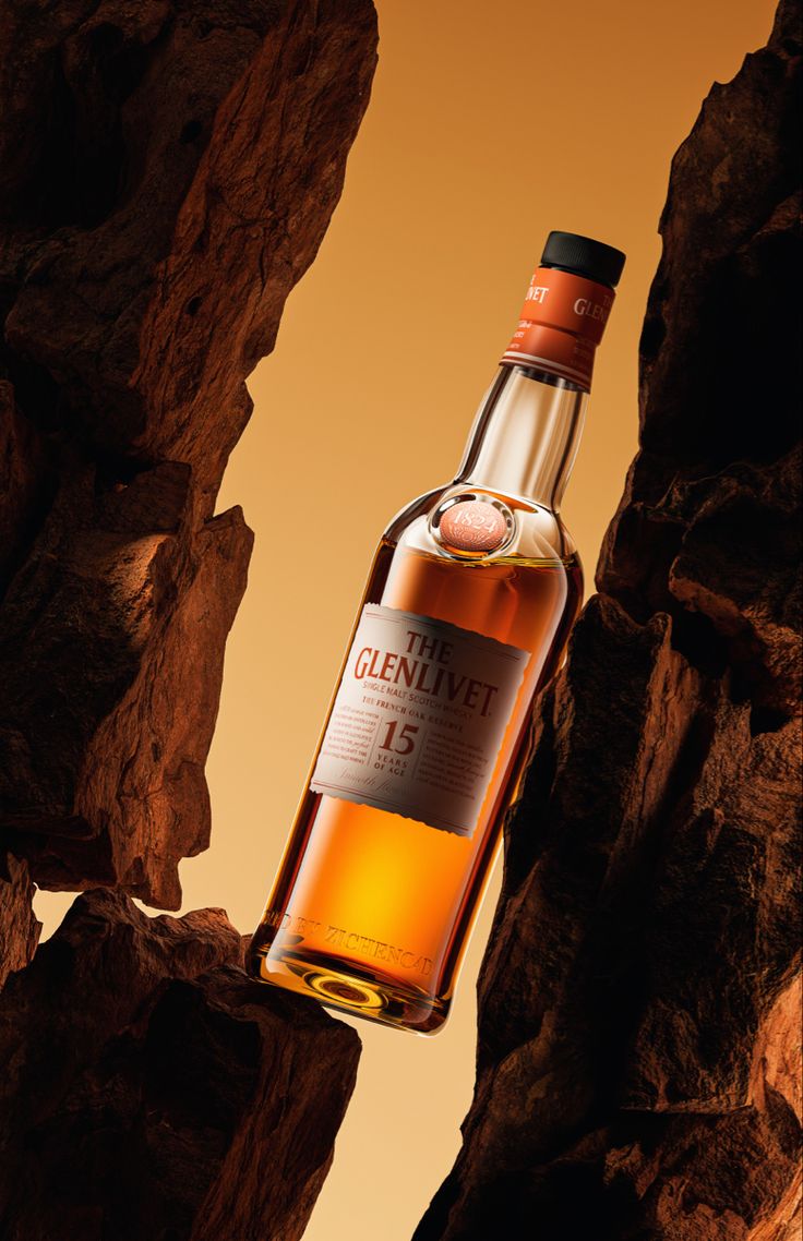 a bottle of whisky sitting on top of a rock formation in front of an orange sky