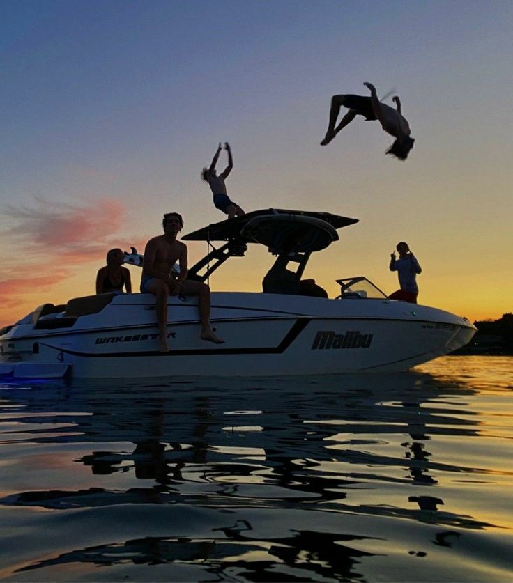 two people jumping off the back of a boat into the water at sunset, while another person dives