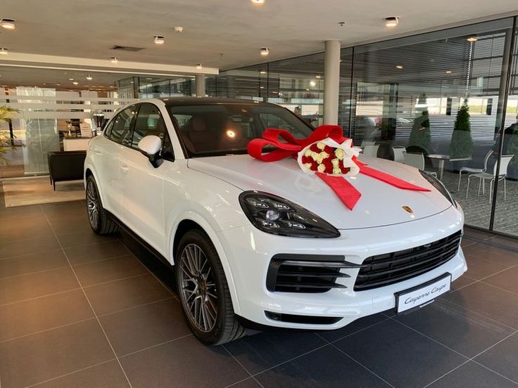 a white porsche cayen with a red bow on it's hood in a showroom