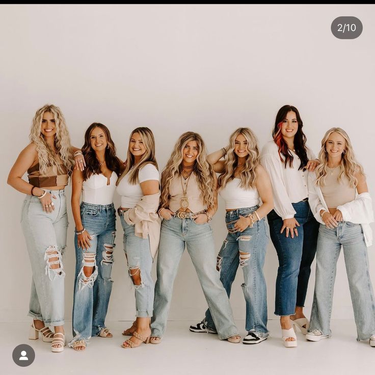 a group of women standing next to each other in front of a white wall wearing ripped jeans