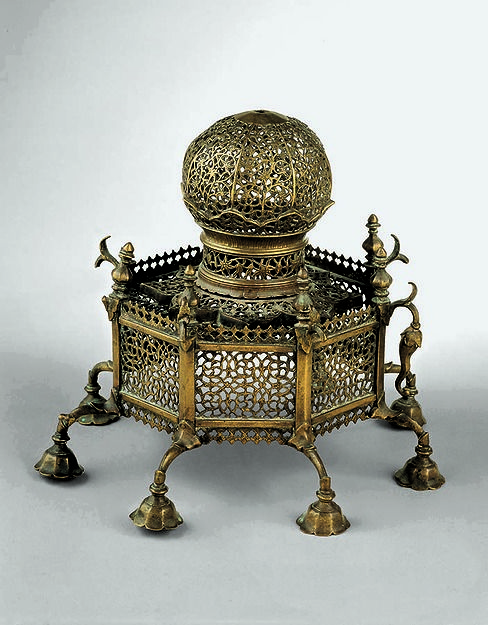 an ornately decorated metal stand with two candles on it's legs and one candle holder in the shape of a basket