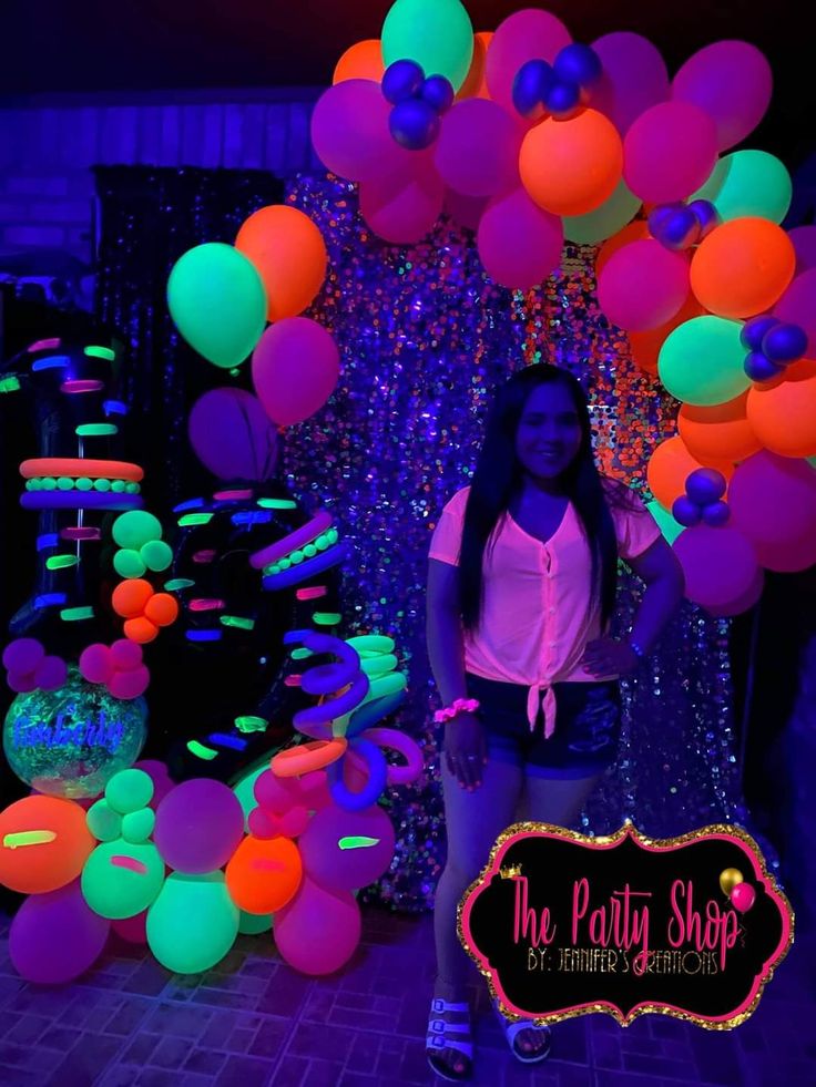 a woman standing in front of neon colored balloons and streamers at the party shop