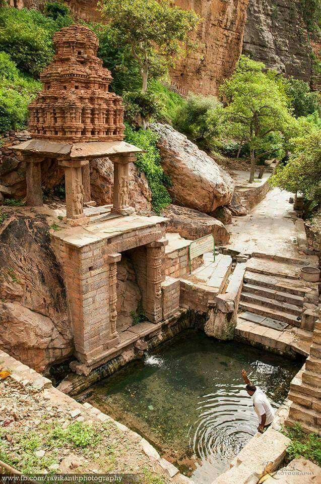 a man standing next to a small pond in the middle of a cliff side area