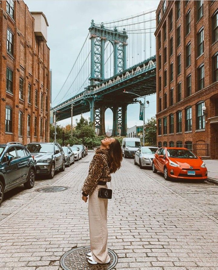 a woman is standing on the sidewalk in front of some cars and a large bridge