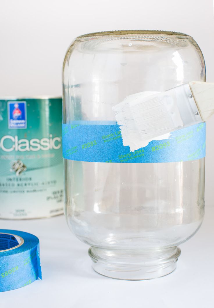 a glass jar filled with water next to a roll of tape and a can of paint