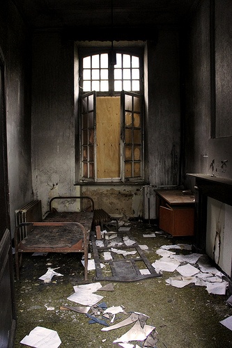 an old run down room with sheets of paper on the floor and a bed in it