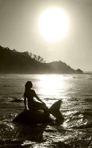 a woman sitting on top of a surfboard in the ocean under a bright sun