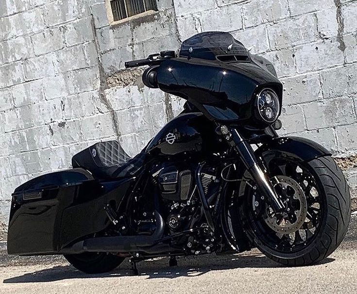 a black motorcycle is parked in front of a brick wall with a window on it