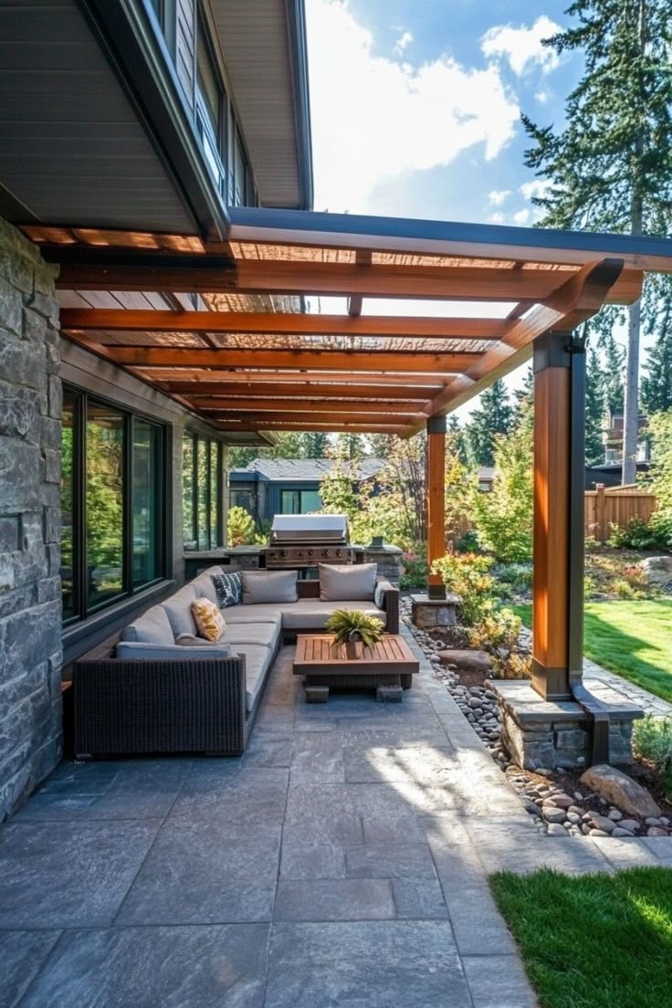 A modern outdoor patio with a pergola, cushioned seating, and a coffee table, set against a lush garden background. Outdoor Patio Awning Ideas, Backyard With Covered Patio, Covered Patio Off House, Backyard Patio With Roof, Outside Veranda Ideas, Backyard Covered Deck Ideas, Cozy Covered Patio Ideas, Backyard Roof Ideas Patio, Patio Addition Ideas Covered