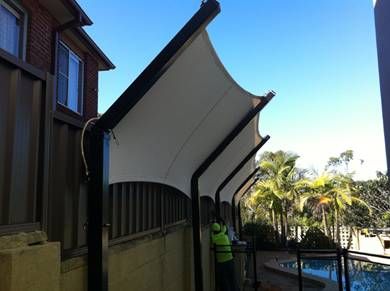 a man standing next to a swimming pool in front of a building with a white awning