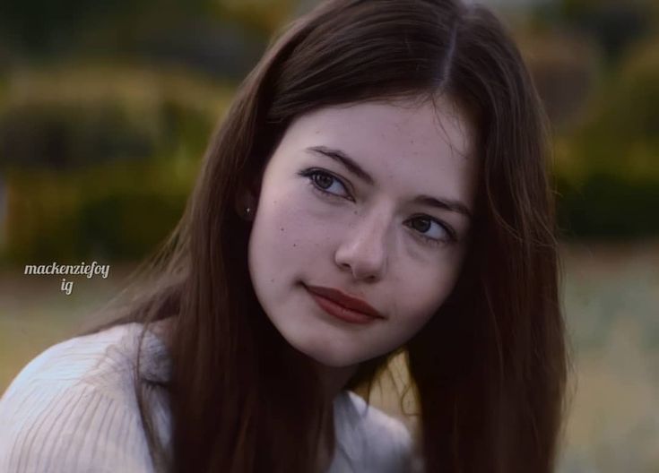 a young woman with long brown hair and blue eyes is looking at the camera while wearing a white sweater