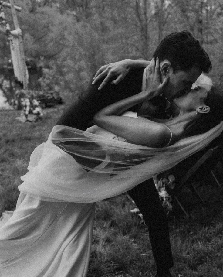 a bride and groom kissing on a park bench