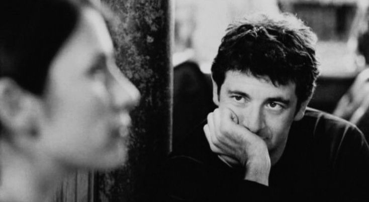 black and white photo of man looking at himself in mirror with his hand on his chin