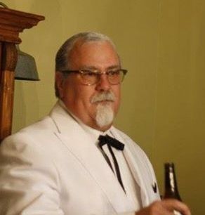 an older man in a white suit holding a beer