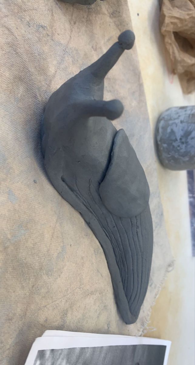 a clay sculpture of a cat laying on the ground next to a book and some rocks