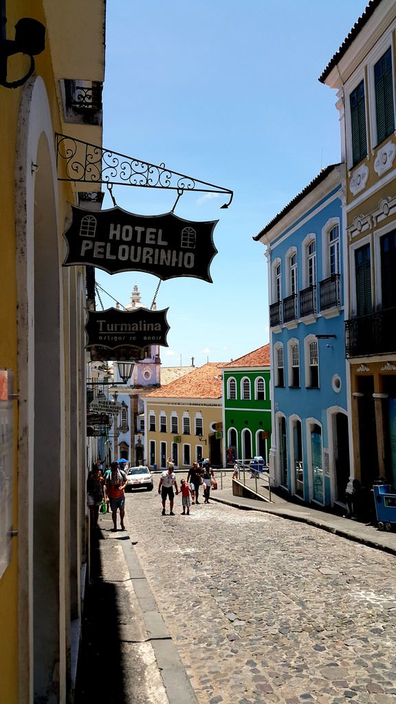 people are walking down the cobblestone street in front of colorful buildings and shops