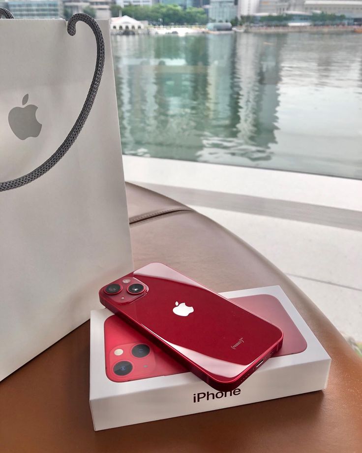 two red iphones sitting on top of a table next to a white paper bag