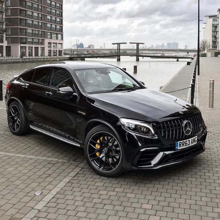 a black mercedes benz suv parked in a parking lot next to some water and buildings