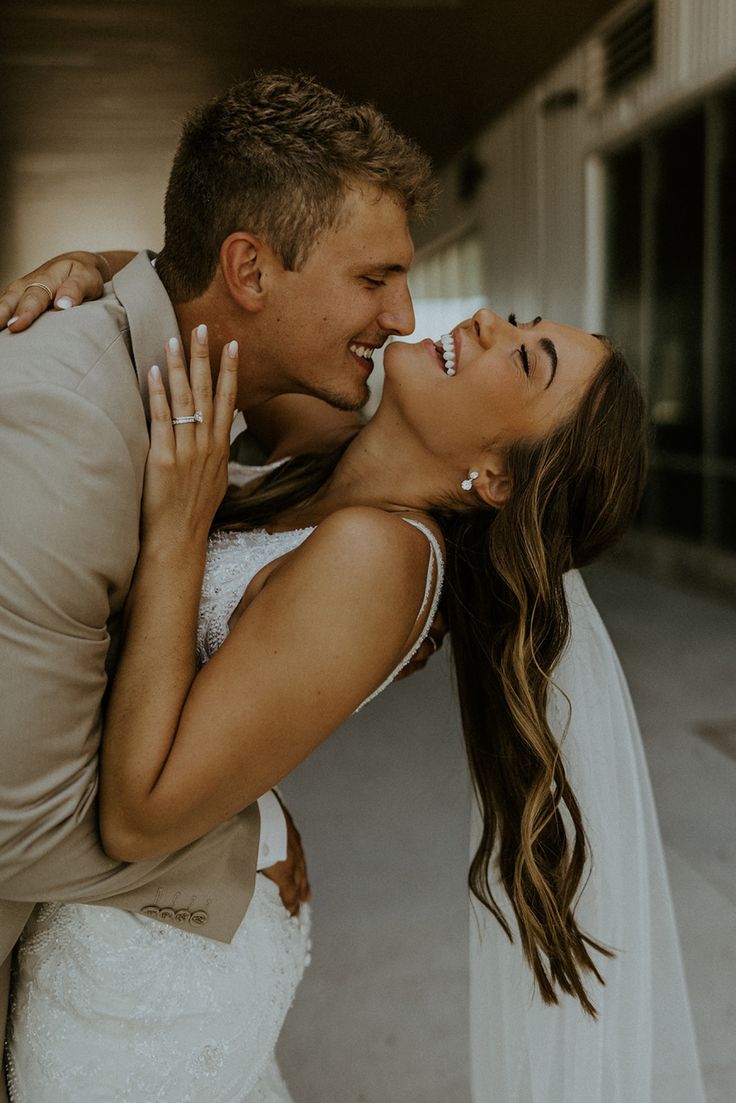 a bride and groom kissing each other in front of an open air building with their arms around each other