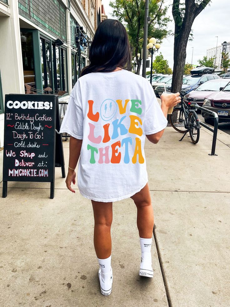 a woman is walking down the sidewalk with her back to the camera and wearing a t - shirt that says love like them